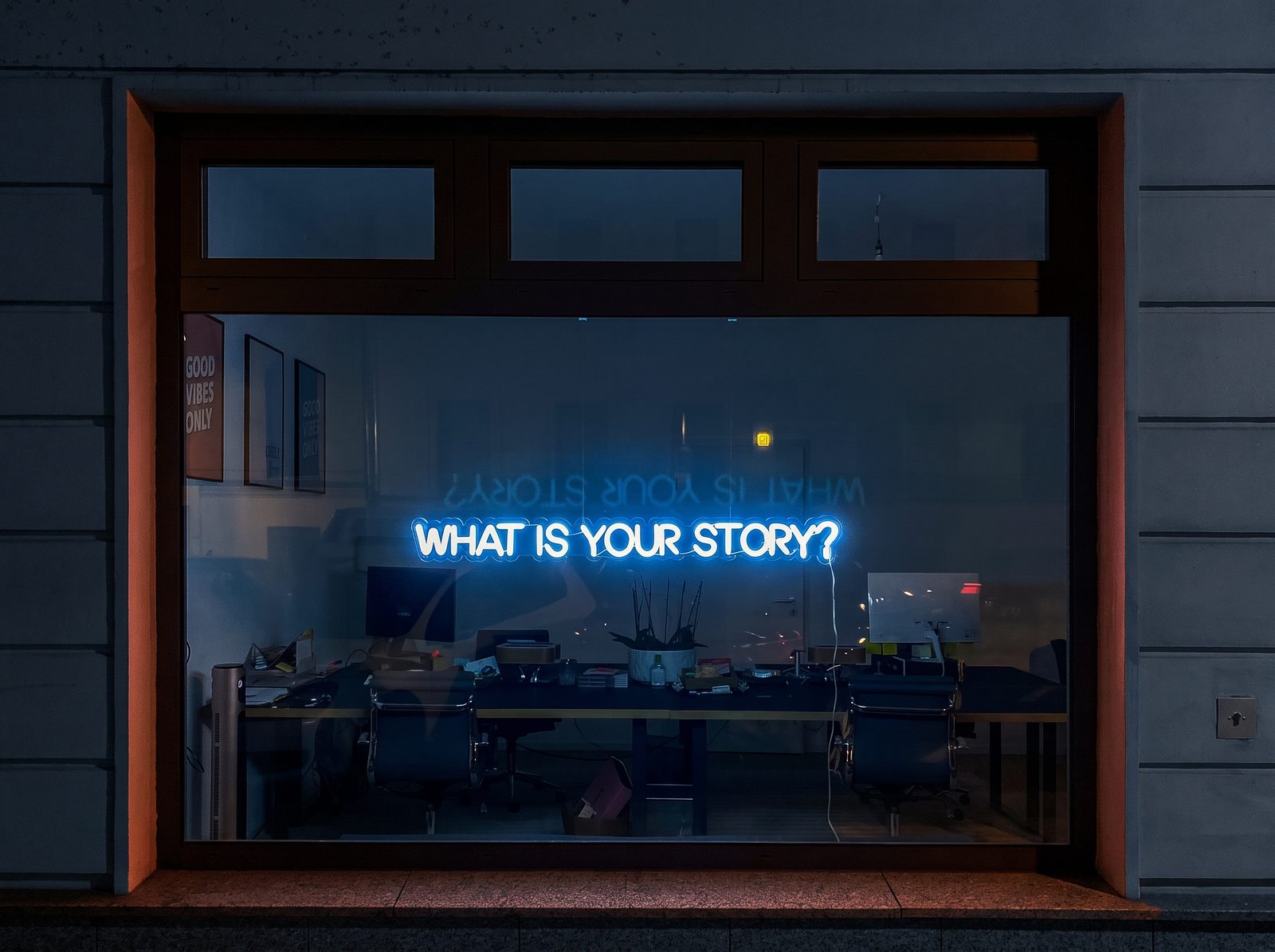 Neon sign in an office window reading: What is your story?